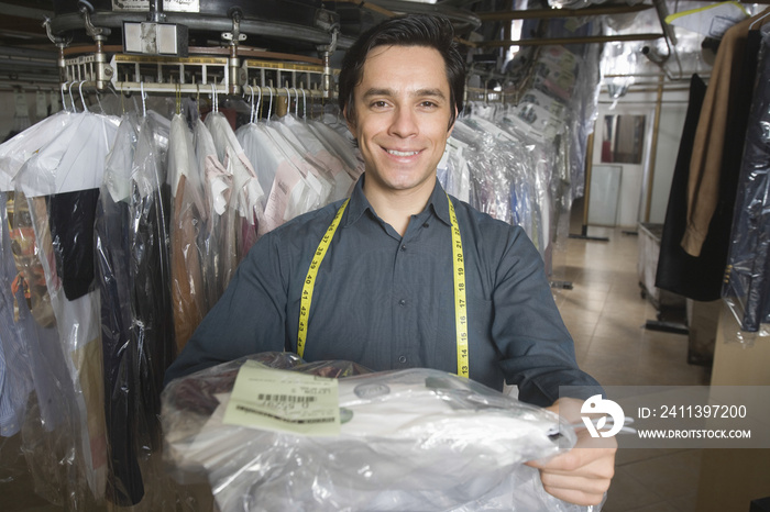 Portrait of confident young owner giving dry cleaned clothes in laundry