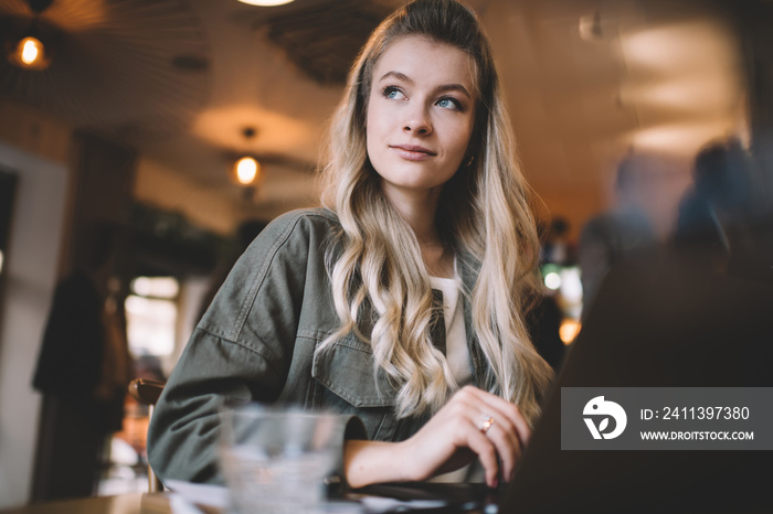 Pensive female sitting in cafe and using laptop while working