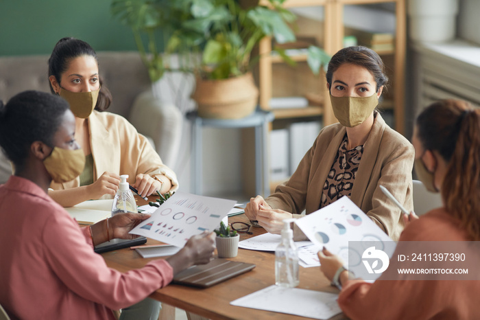 High angle view at multi-ethnic group of young businesswomen wearing masks during meeting in office, copy space