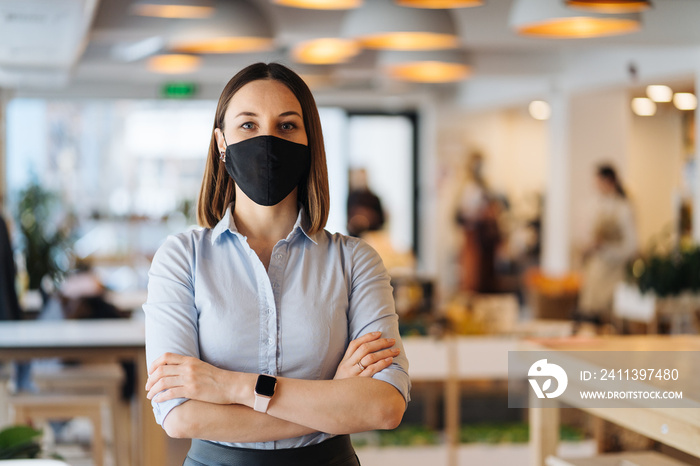 Woman business owner wearing face mask after reopening restaurant, arms folded