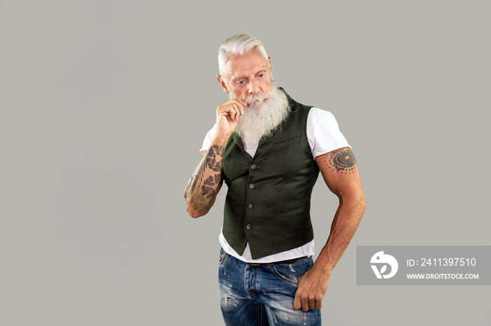 Bearded and tattooed senior fashionable man in stylish clothing posing in studio.