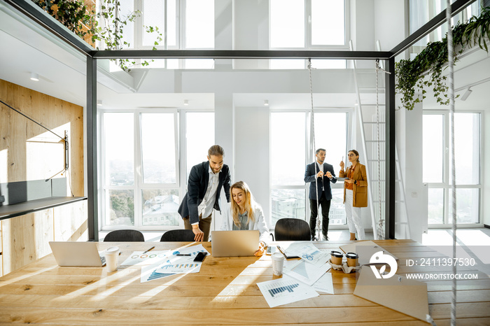 Office employees talking and having some office work at the large meeting table, wide view on the spacious room with large windows