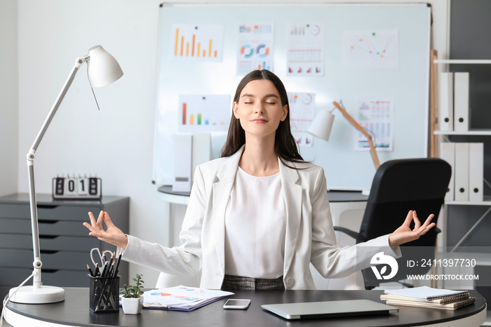 Young businesswoman meditating in office