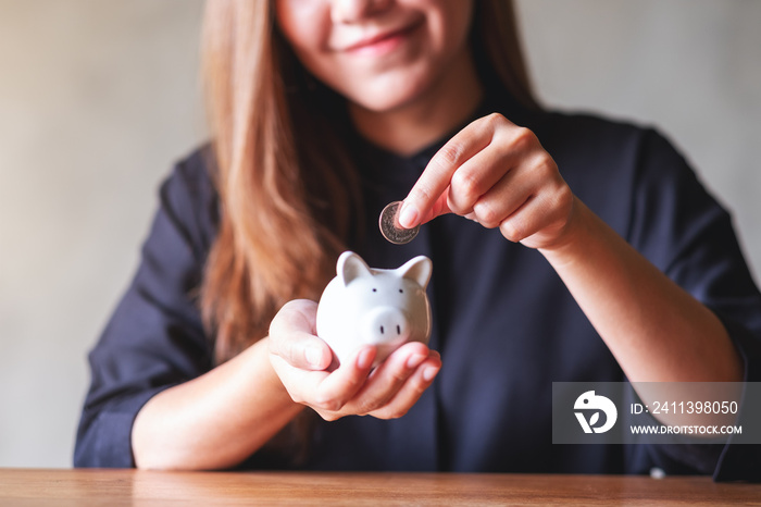 Closeup image of a young woman holding and putting coins into piggy bank for saving money concept