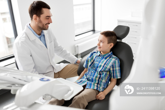 medicine, dentistry and healthcare concept - male dentist talking to kid patient at dental clinic