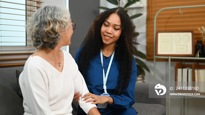 Elderly woman talking with caring young nurse, receiving home care physical and moral support. Home health care service concept