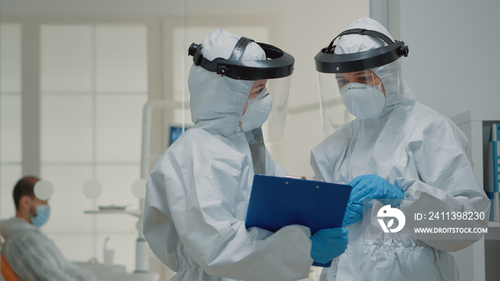 Close up of dentistry doctors talking wearing hazmat suit with face shield, mask, and coverall. Caucasian dentist team discussing dental operation and consultation for teeth protection