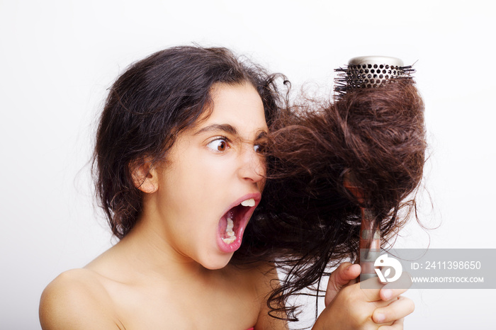 Hair care concept with portrait of girl brushing her unruly, tangled long hair isolated on white