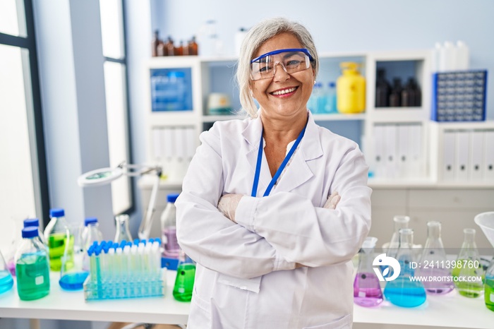 Middle age woman wearing scientist uniform standing with arms crossed gesture at laboratory