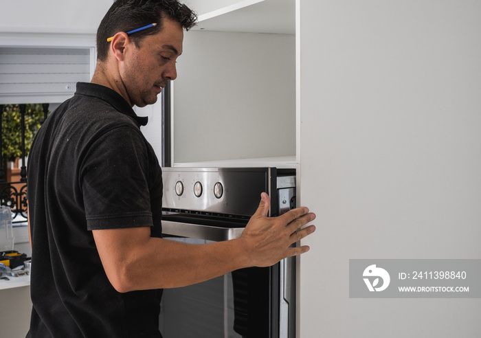 Man placing an oven inside the hole of a new kitchen cabinet