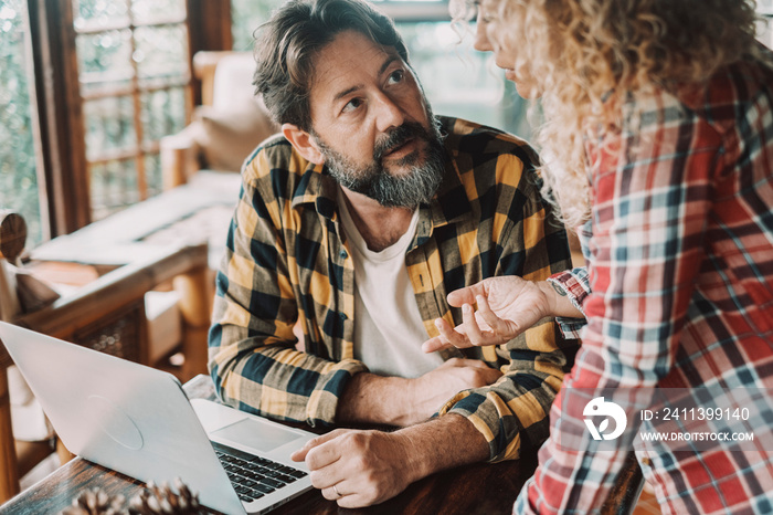 Adult couple at home discussing together at the table. Man using computer and looking woman explaining and talking. Two people male and female in indoor activity. Married life. Relationship problems