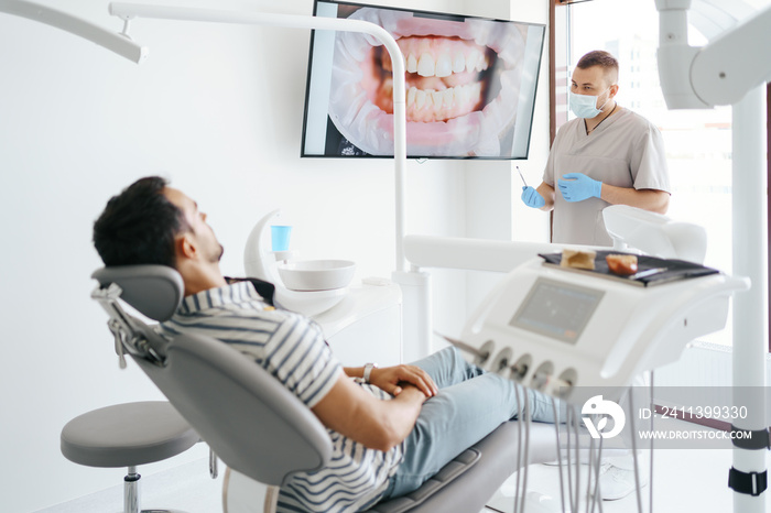 Dentist discussing with laying patient showing the image of his teeth on the screen