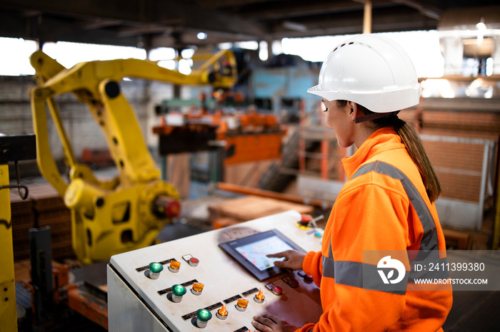 Female industrial worker in safety uniform and hard hat operating manufacturing machine via control panel.