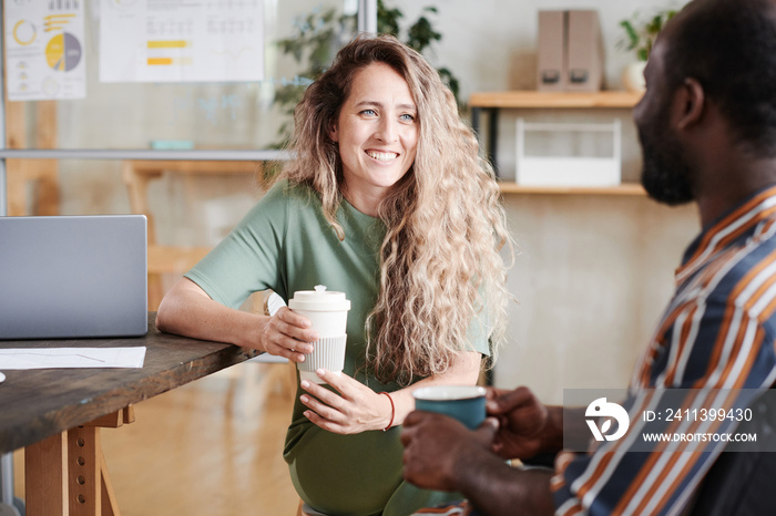 Young smiling businesswoman drinking coffee with her colleague at office during coffee break