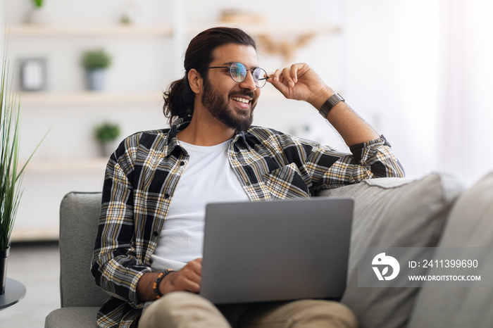 Dreamy arab guy freelancer working from home, using laptop