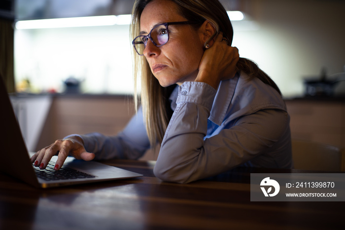 Pretty, middle-aged woman working late in the day on a laptop computer at home, running a business from home, working remotely - getting frustrated