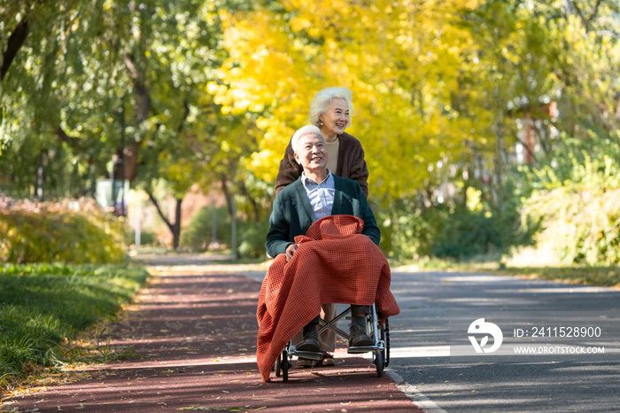 老年女人推着坐轮椅的老伴散步