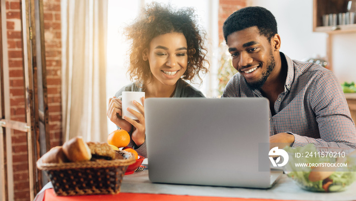 Couple using laptop, having coffee in kitchen