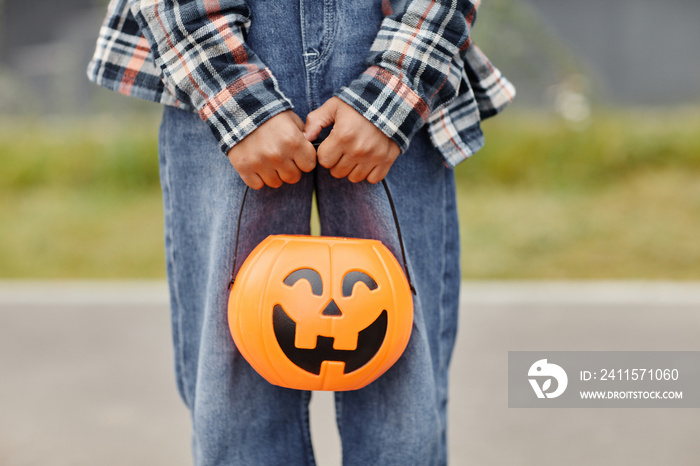 Close up of unrecognizable boy holding pumpkin shaped Halloween pail outdoors, copy space