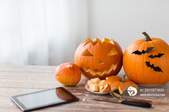 holidays, halloween and technology concept - jack-o-lantern or carved pumpkin with tablet pc compute