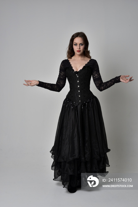 full length portrait of brunette girl wearing long black gown with corset. standing pose on grey stu