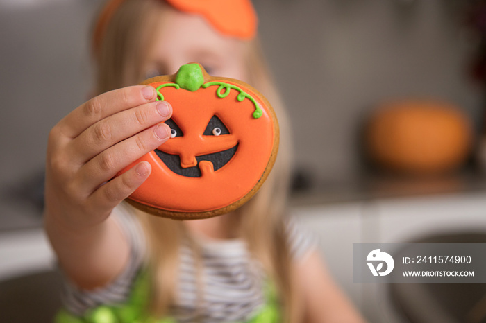 A little girl shows a gingerbread pumpkin close-up in Halloween style.