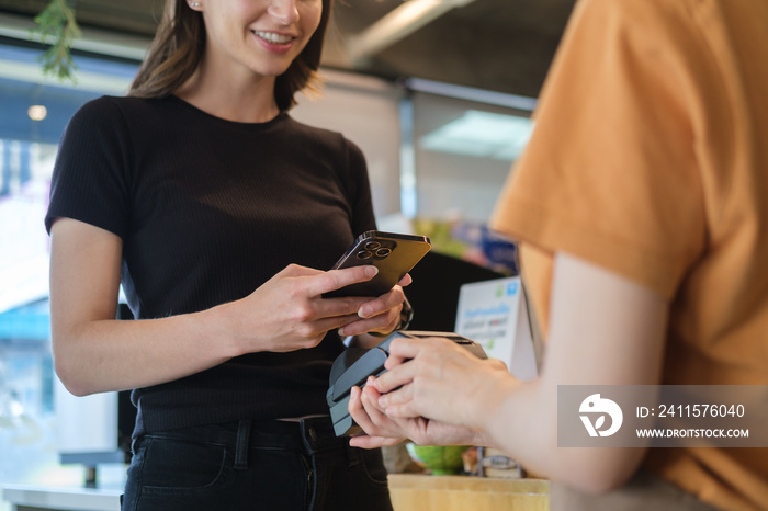 Smiling female customer using smart phone scan QR code for payment at coffee shop. NFC contactless p