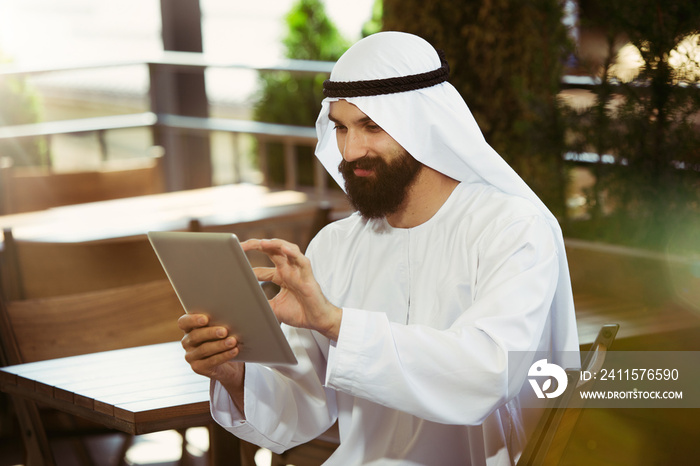 Arab saudi businessman working online with a laptop and tablet in a coffee shop or a cafe with an ou