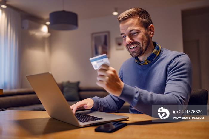 Debit, credit card, online banking, and shopping. A happy young man is sitting in his living room at