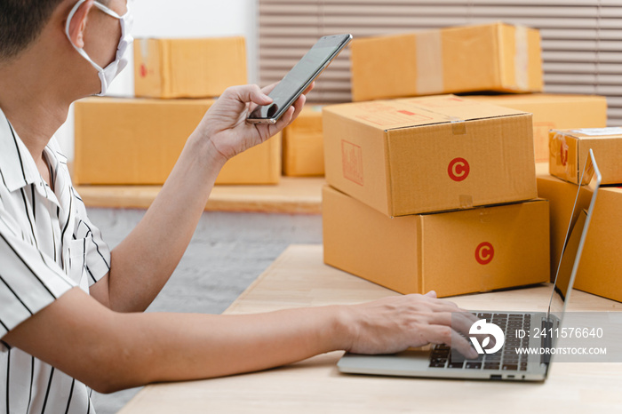 Young teenage man as freelance working with laptop computer and packing of postal parcel box in livi