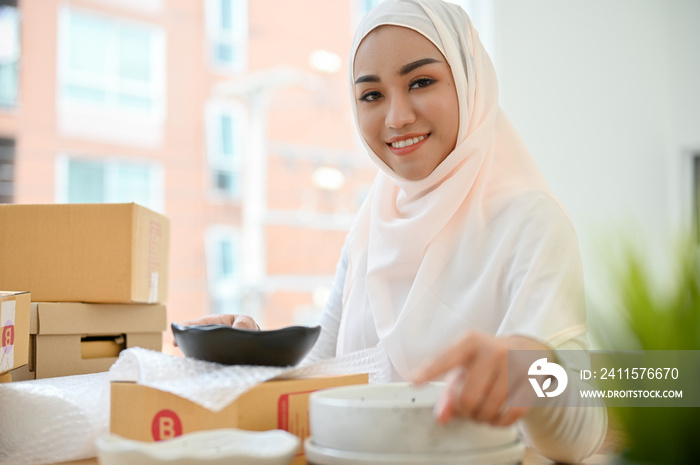 Muslim female SME entrepreneur preparing order, packing a product into a shipping box