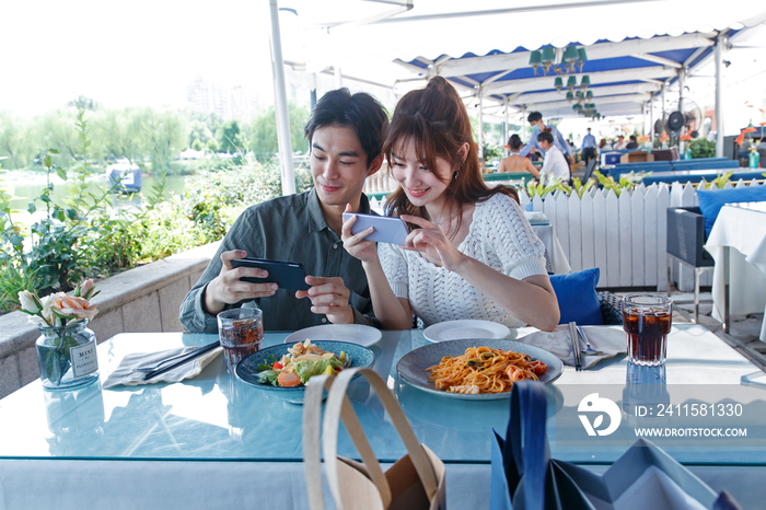 青年情侣在餐厅里用手机拍照