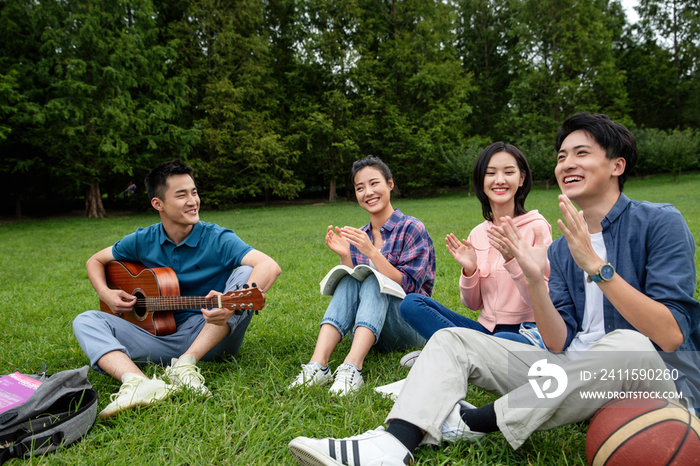 快乐的大学生在草地上弹吉他唱歌