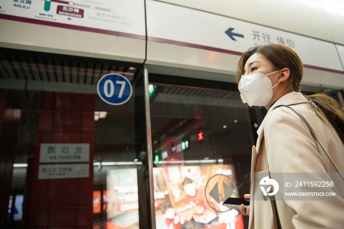 戴口罩的年轻女人站在地铁站台上