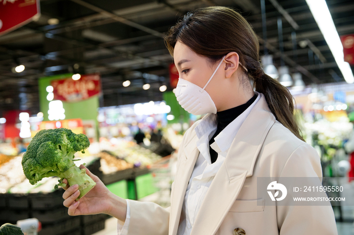 戴口罩的青年女人在超市购买蔬菜