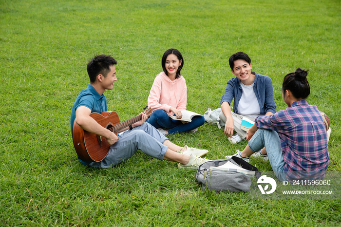 快乐的大学生在草地上弹吉他唱歌