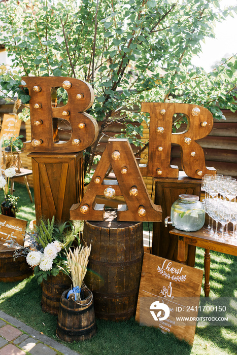 The bar area at the summer party is decorated with wooden letters with bulbs and flowers. Many glasses and drinks on the table