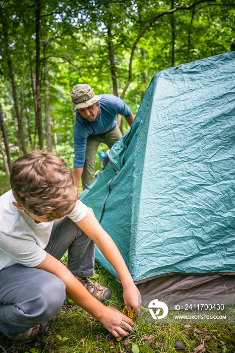 Air Force service member sets up a tent with his sons on  a backpacking trip.