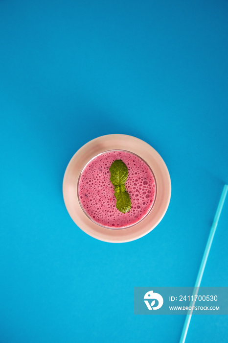 Fresh and delicious drink full of vitamins and antioxidants based on mixed red fruits on a blue background. Red fruit smoothie with mint. Top view and copy space.