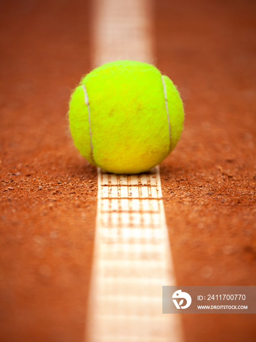 A yellow tennis ball lies on the clay court.