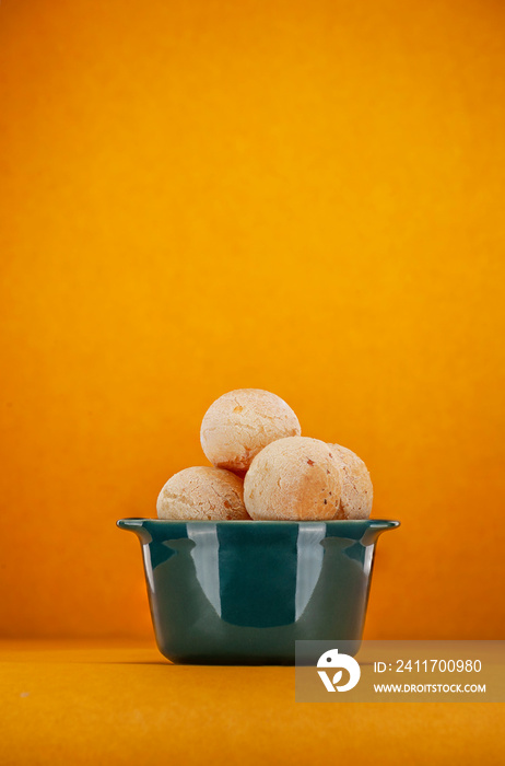 Isolated cheese breads in a green ramekin on orange background.