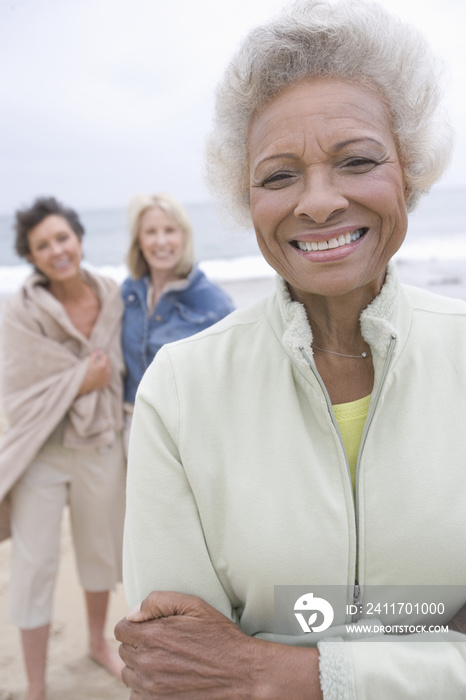 Portrait of a cheerful senior woman stands in fleece jacket with friends on beach