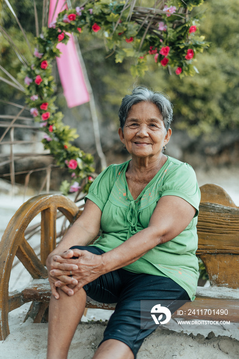 A Beautiful Portrait of a Gorgeous Asian Filipino Grandmother sitting on a Bench while on a Holiday Summer Vacation on an Exotic Island in the Philippines