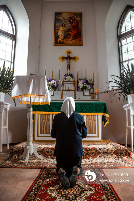 Old woman in a white scarf on a knees pray at the altar of the Catholic Church