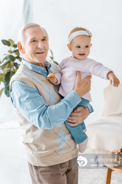 senior grandfather holding toddler granddaughter with cookie