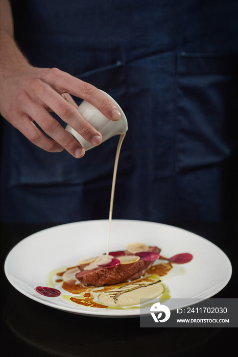 Chef pouring sauce on baked duck breast with beetroot and daikon