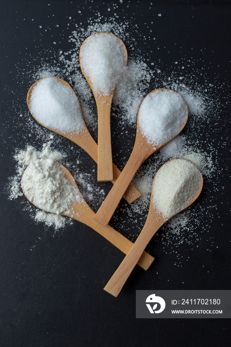 Salt, sugar, flour on bamboo wooden spoons, arranged like a flower on a black background