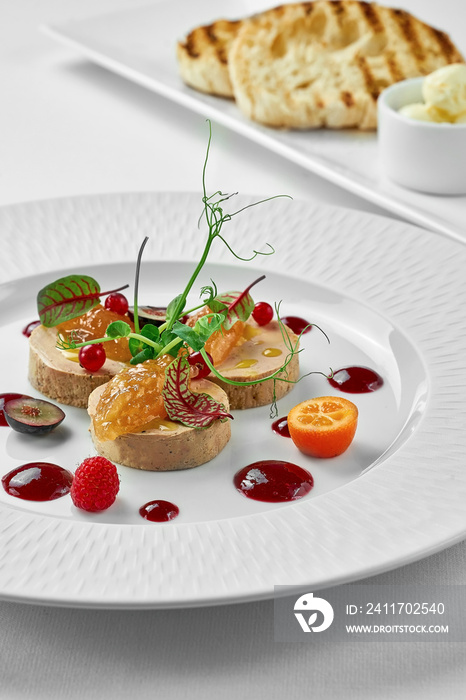 Foie gras with apple confit and berry sauce in a white plate on a white background. Close-up, selective focus.