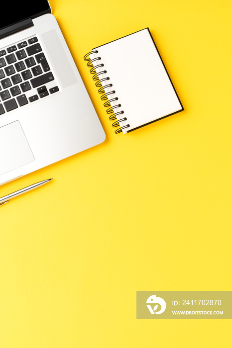 Elegant office desktop with laptop, notebook and pen on yellow background with copyspace. Modern workspace