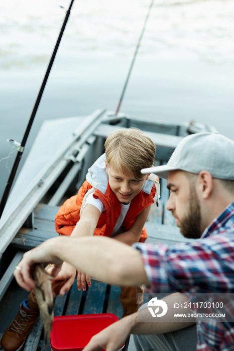 Father and son catching a fish while they fishing on the boat on the lake